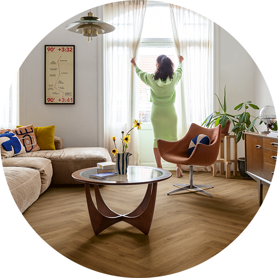 Žena rozhrnuje závěsy v obývacím pokoji s vinylovou podlahou se vzorem rybí kosti